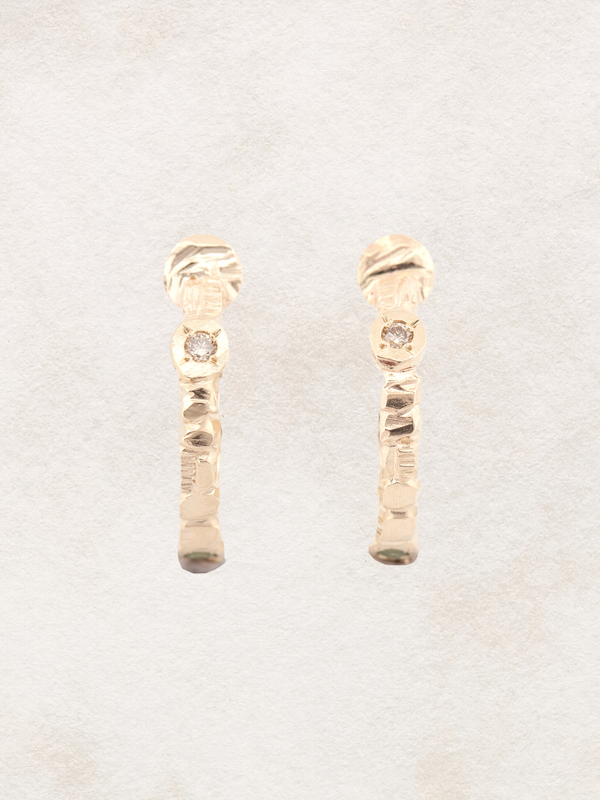 Gold earrings with a textured design on a light gray background